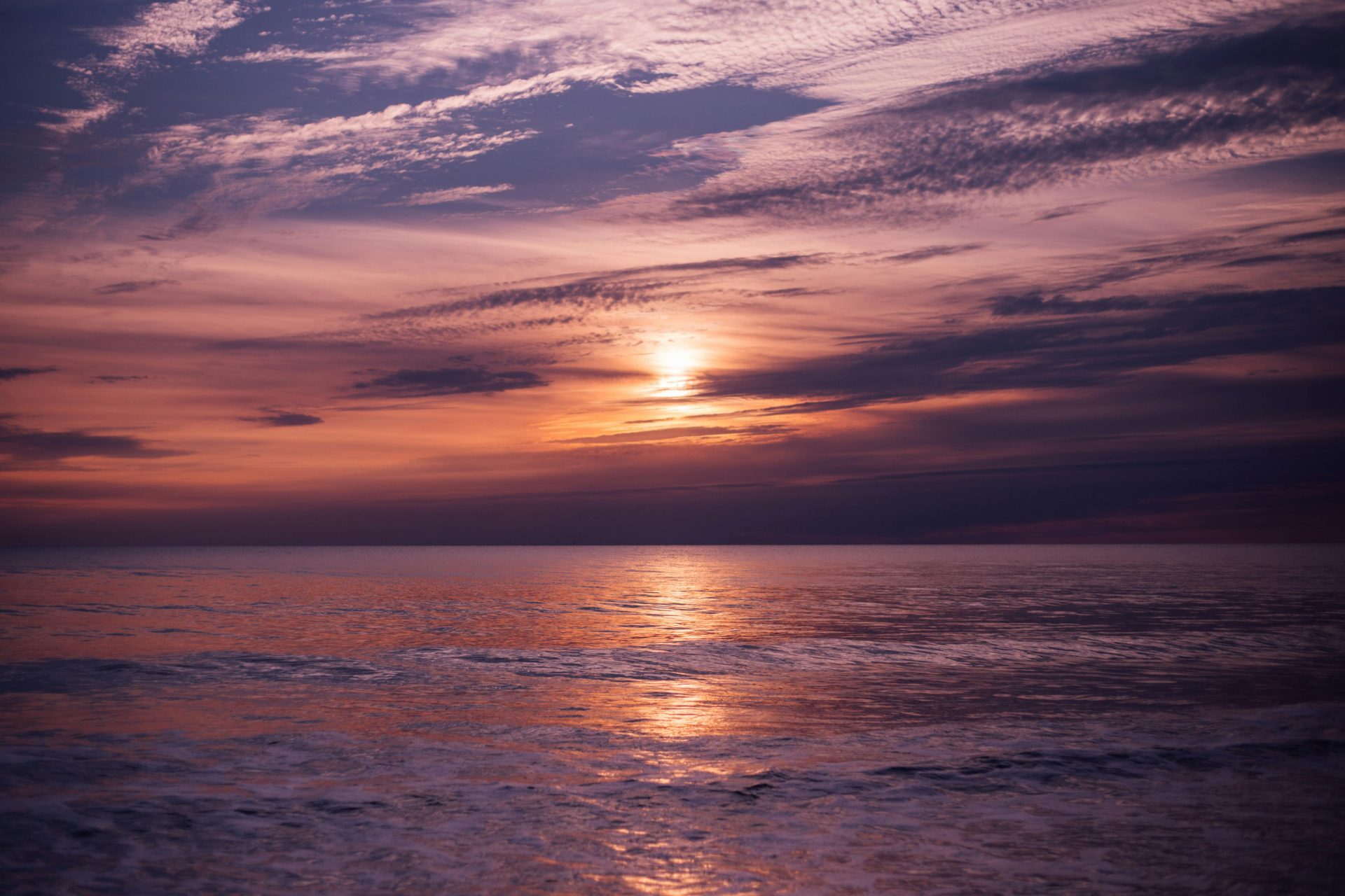A breathtaking ocean sunset with vibrant pink and purple hues reflecting on calm waters, creating a serene atmosphere.