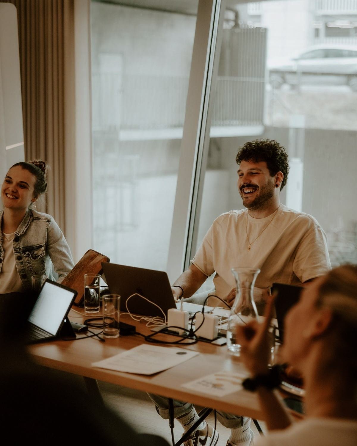 Réunion de travail : Un groupe de jeunes professionnels discutant et souriant autour d'une table dans un bureau.