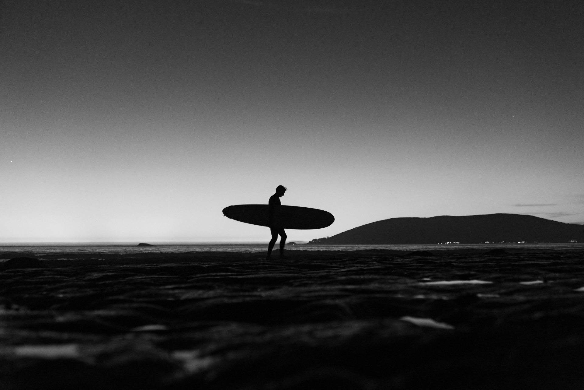 Silhouette au crépuscule : Une personne marchant seule sur une plage sombre face à la mer à la tombée de la nuit.