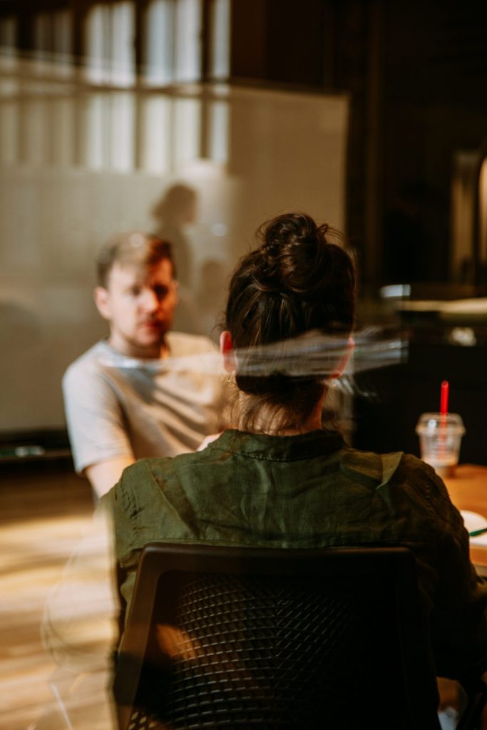 Discussion professionnelle : Deux personnes discutant sérieusement face à face dans un espace de travail chaleureux.